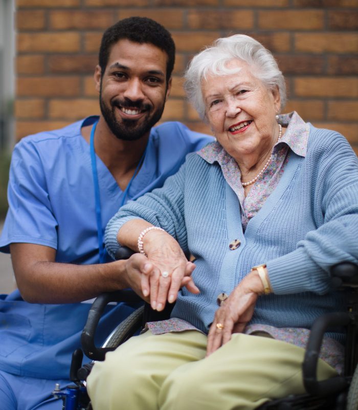 Happy senior woman at a wheelchair spending time outside with her assistant.